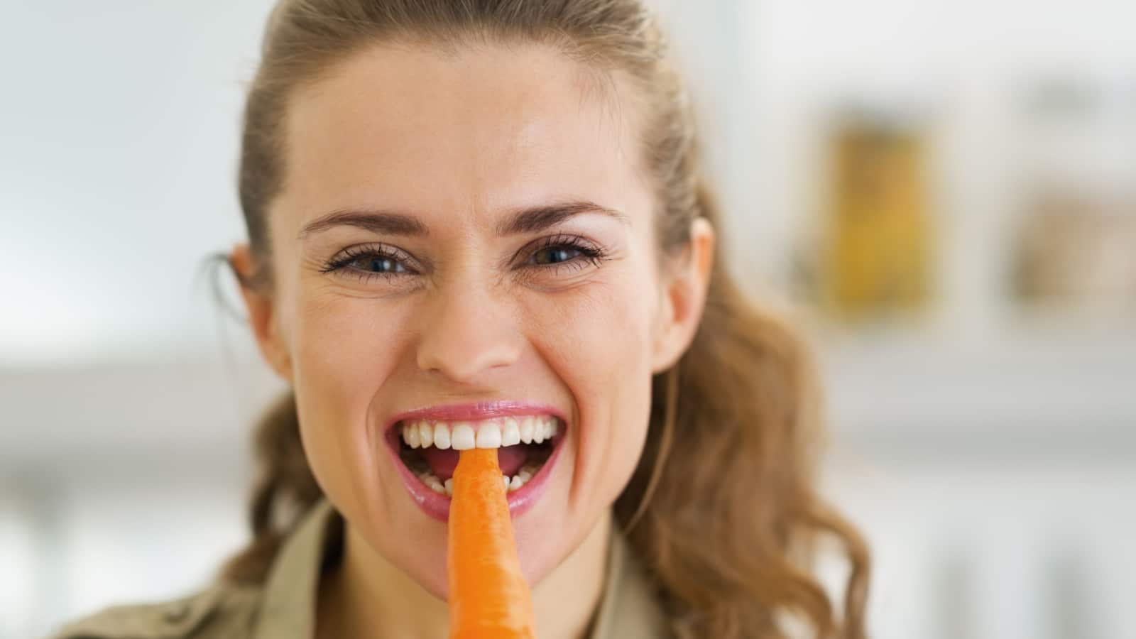 happy woman eating carrot Shutterstock